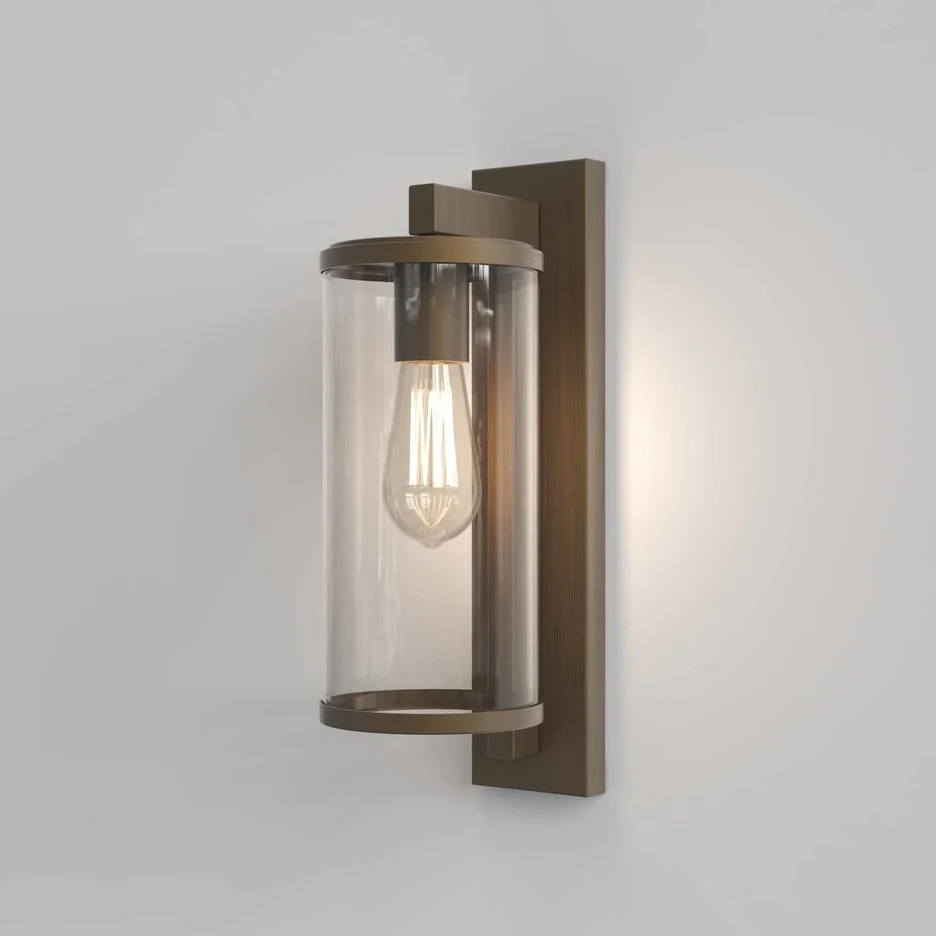 The Pimlico wall light is an outdoor light that features cylindrical glass against a rectangular backing in a bronze finish.