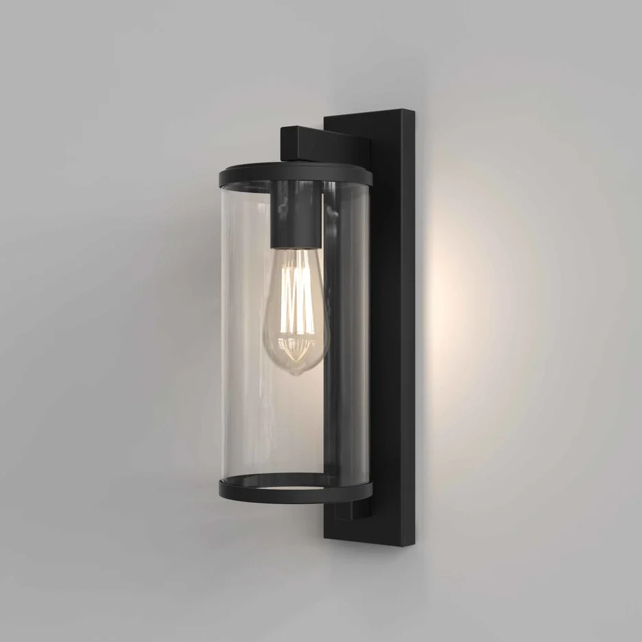 The Pimlico wall light is an outdoor light that features cylindrical glass against a rectangular backing in a textured black finish.