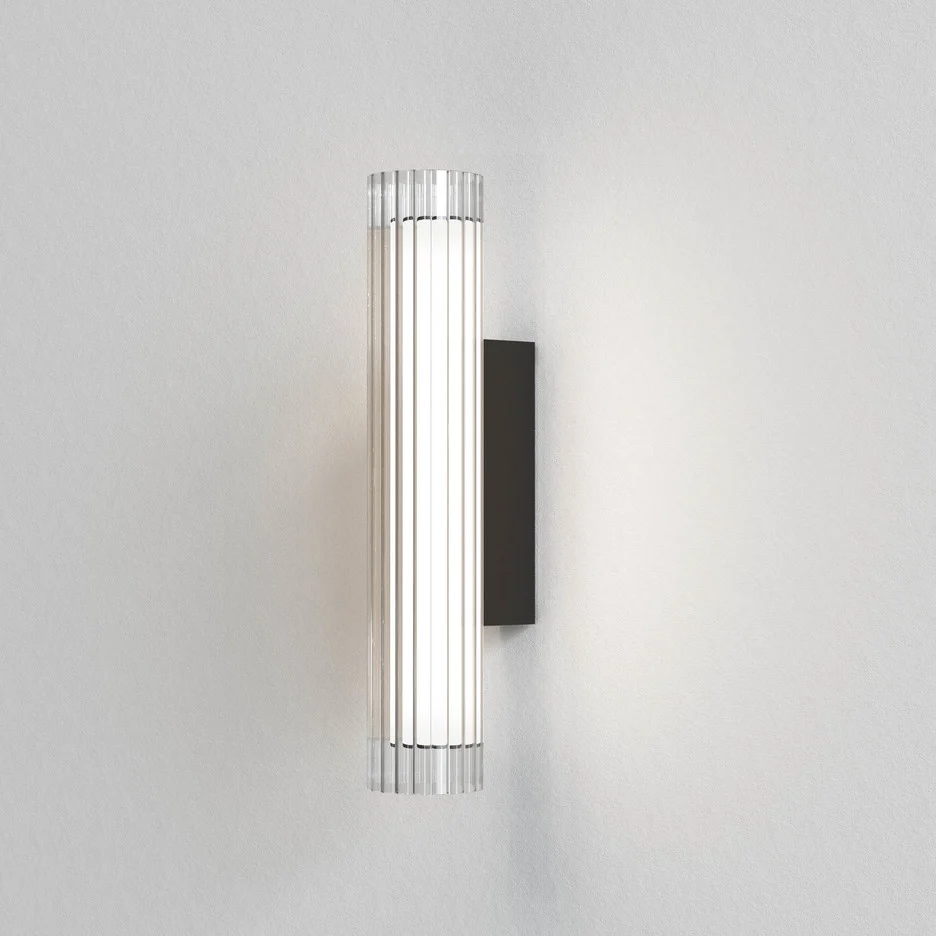 The io wall light features a modern cylindrical design with ribbed glass in a textured black finish. IP44 rated and safe for use and bathrooms.