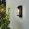 The Pimlico wall light is an outdoor light that features cylindrical glass against a rectangular backing in a textured black finish. Shows the fitting installed outdoors.