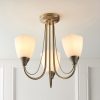 Shows the Haughton ceiling light installed in a room and turned on. The light features 3 arched arms finished in antique brass, complete with opal glass shades.