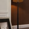 Shows the Corvina floor light on in a room. The light features a stylish design with a dark wooden tapered stand, bright nickel base, and mink faux shade.