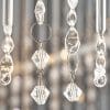 Close up of the Camille pendant light's clear glass beads. The pendant is a stunning chandelier with 24 lamps, featuring a mix of glass rods and faceted glass beads. Multiple rings support the delicate glass detailing in a sleek chrome finish.