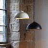 Shows both the Colman pendant lights hanging in a rustic brick room. One pendant features a gloss cream finish, and the other features a matt black finish, both have a shimmering gold leaf finish on the interior that adds a splash of colour.