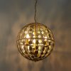 Shows the lighting effect of the Alvah pendant light. The pendant features a delicate cage design with decorative circle cut outs enclosing 3 centre lamps. The metalwork comes in a luxuriant gold leaf finish.