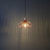 The Kimberley pendant light against a dark wall, showing the lighting effect created by the shade. The pendant features an elegant industrial design with a metal wire shade finished in polished copper plate.