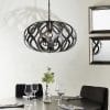 Shows the Sirolo pendant light hanging over a dining room table. The pendant features overlapping abstract waves finished in antique brushed bronze enclosing 5 lamps.