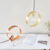 Shows the Hoop pendant light in a brass plated finish installed over a desk where the Hoops table lamp in brushed copper is set on.