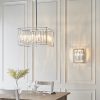 Shows the Acadia pendant light hanging in a room alongside the Acadia wall light. The pendant features high quality bevelled glass crystals enclosed in a polished chrome frame with 6 lamps.