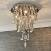 Shows a close up of the Melody ceiling light in a room, showing the lighting effect. Features a tiered design with hanging crystal glass beads and teardrops alongside chrome, leaf shaped details enclosing 3 lamps.