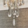 Close up of the bottom of the Melody ceiling light and the hanging crystal glass beads and teardrops alongside chrome, leaf shaped details enclosing 3 lamps.