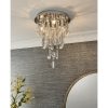 Shows the Melody ceiling light in a room, showing the lighting effect. Features a tiered design with hanging crystal glass beads and teardrops alongside chrome, leaf shaped details enclosing 3 lamps.