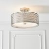 Shows the Cordero ceiling light in a simple white room. Features a satin nickel metal outer shade with a laser cut circle pattern and a white inner fabric shade. The bottom of the inner shade has a frosted glass diffuser enclosing three lamps.