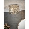 Shows the Fayola ceiling light in an elegant room. Features a modern and striking design. The shade has an intricate laser cut pattern with a chrome finish and premium crystal bejewelled detailing enclosing five lamps.