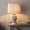 Shows the Mae lampshade, ⌀16 inch, tapered variety fitted onto a table lamp base in a simple room.