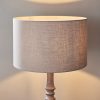 Shows the Mae lampshade, ⌀16 inch, fitted onto a floor lamp base. The lampshade features a contemporary, cylindrical design in taupe natural linen with cotton mix fabric lining and rolled edges.