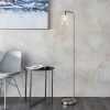 Shows the Toledo floor light in a contemporary room. The light features sleek metal in a brushed nickel finish, supporting a clear glass shade. Complete with inline foot switch.