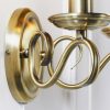 Close up of the Bernice wall light on a plain white wall. The light features two curved arms finished in antique brass, supporting two traditional lampholders on either side. A pull cord switch hangs in the centre.