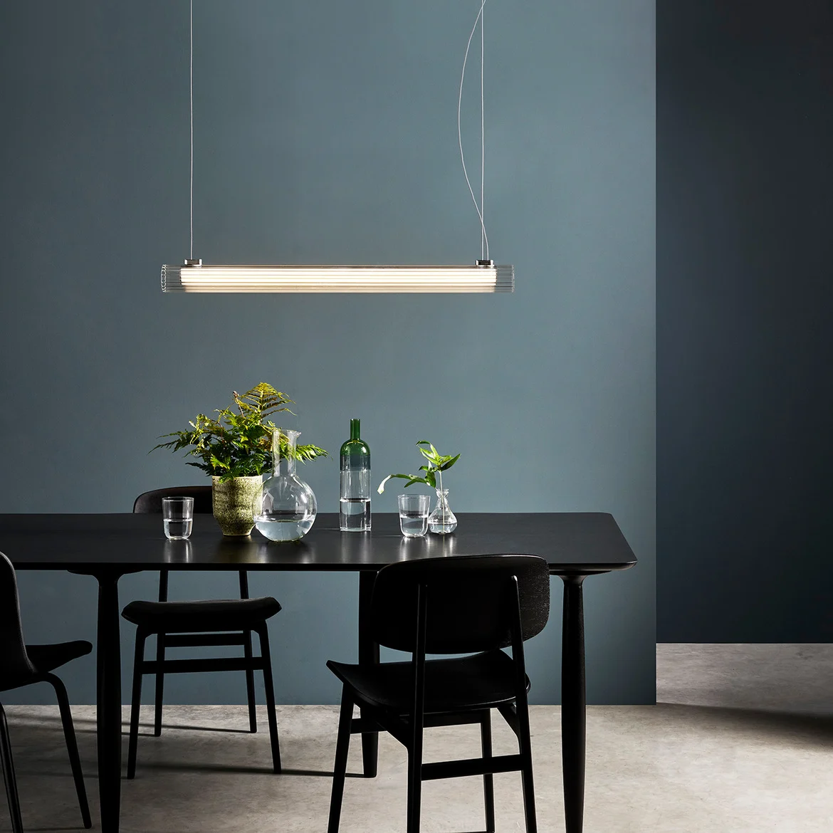 The io pendant light features a modern cylindrical design with ribbed glass and detailing in a polished chrome finish. Shows the pendant hanging over a dining table.